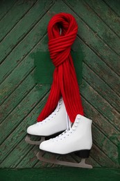 Pair of ice skates with knitted scarf hanging on green wooden wall