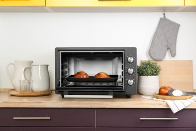 Open electric oven with delicious pastry on wooden table in kitchen