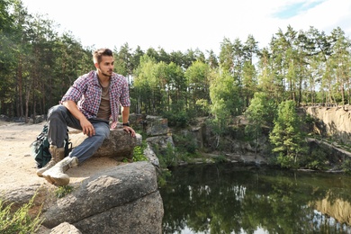 Young man on rock near lake and forest. Camping season