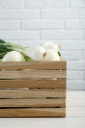 Photo of Crate with green spring onions on white wooden table