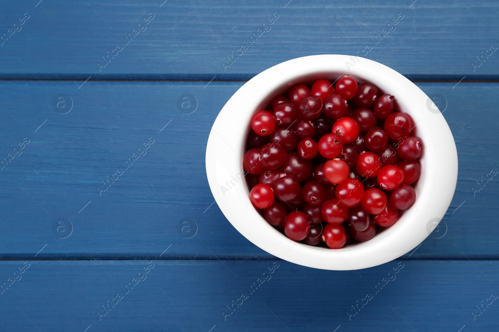 Photo of Fresh cranberries in bowl on blue wooden table, top view. Space for text