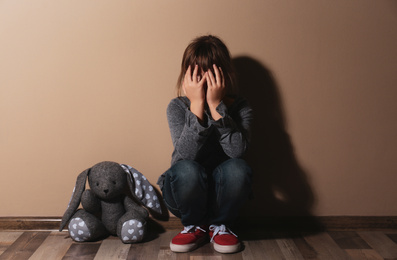 Photo of Abused little girl crying near beige wall. Domestic violence concept