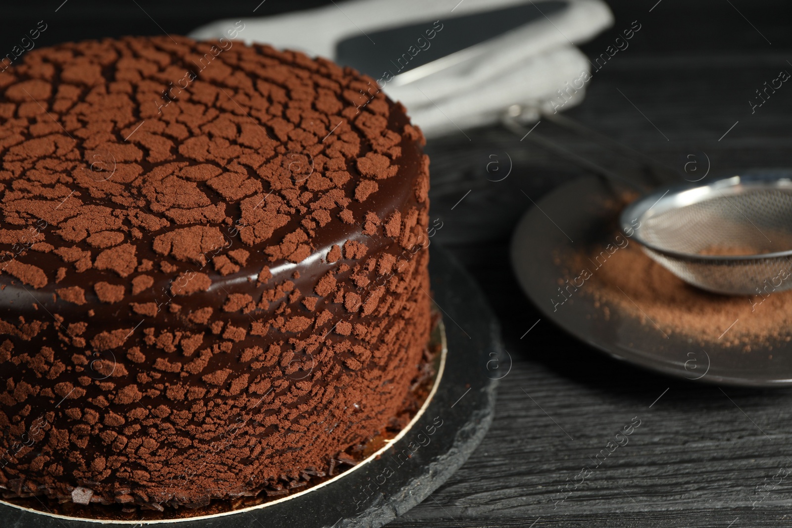 Photo of Delicious chocolate truffle cake and cocoa powder on black wooden table, closeup