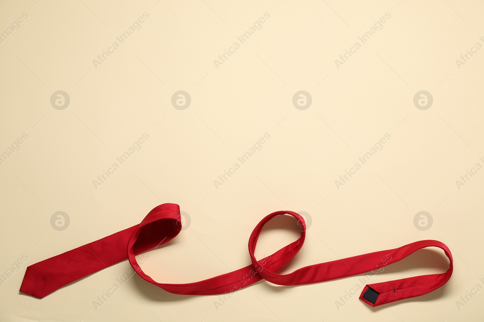 Photo of Red necktie on beige background, top view. Space for text