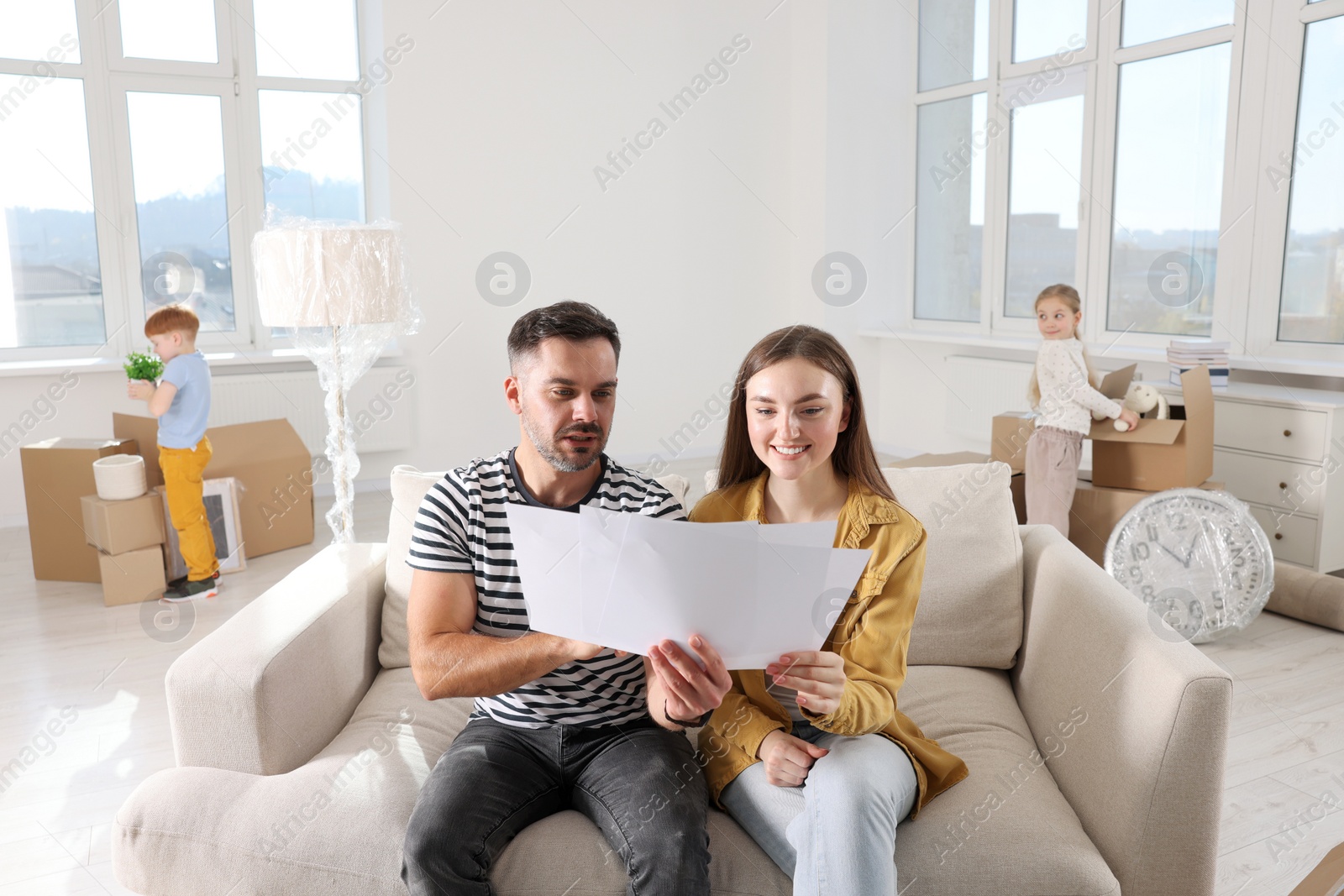 Photo of Family settling into home. Happy wife with husband choosing interior details while daughter and son unpacking boxes in new apartment. Moving day