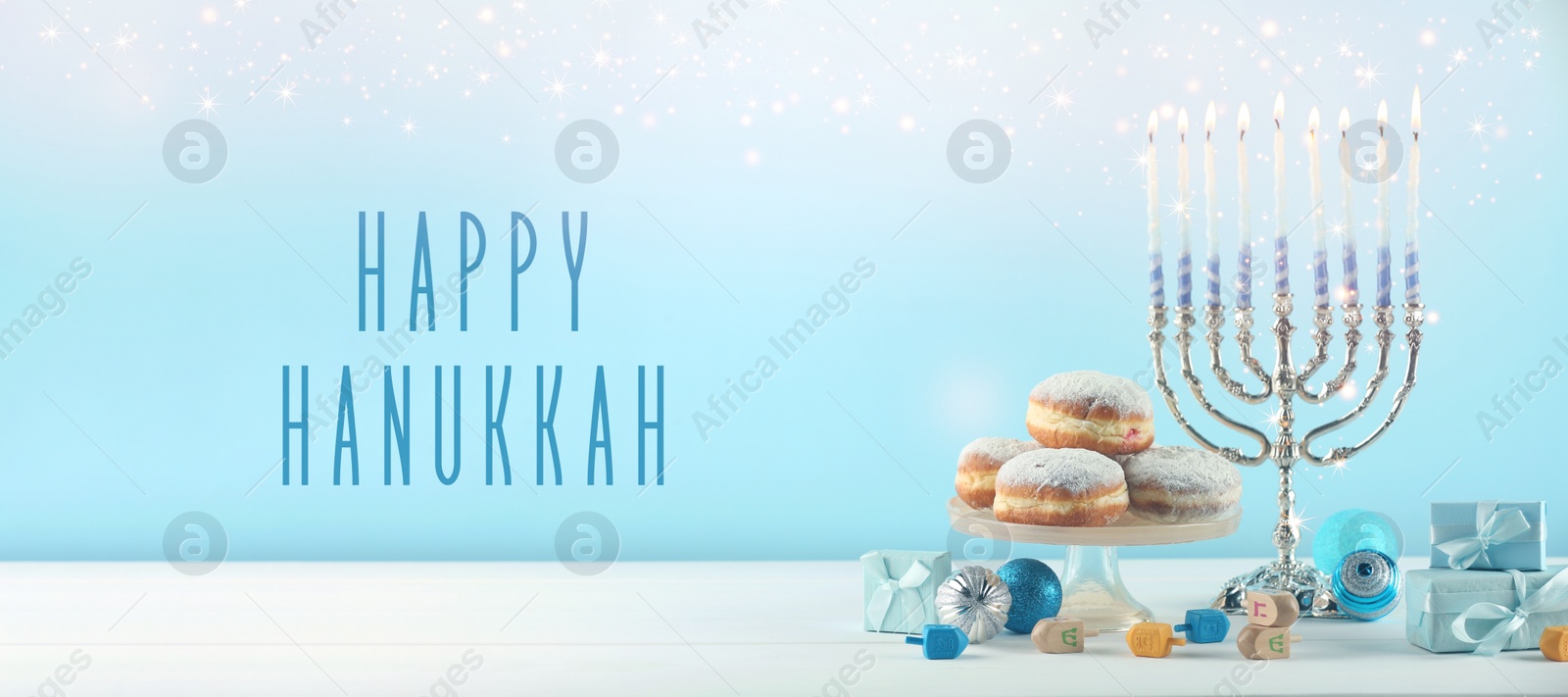 Image of Happy Hanukkah. Menorah, donuts, dreidels and gifts on white table, banner design