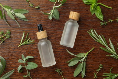 Bottles of essential oil and fresh herbs on wooden table, flat lay