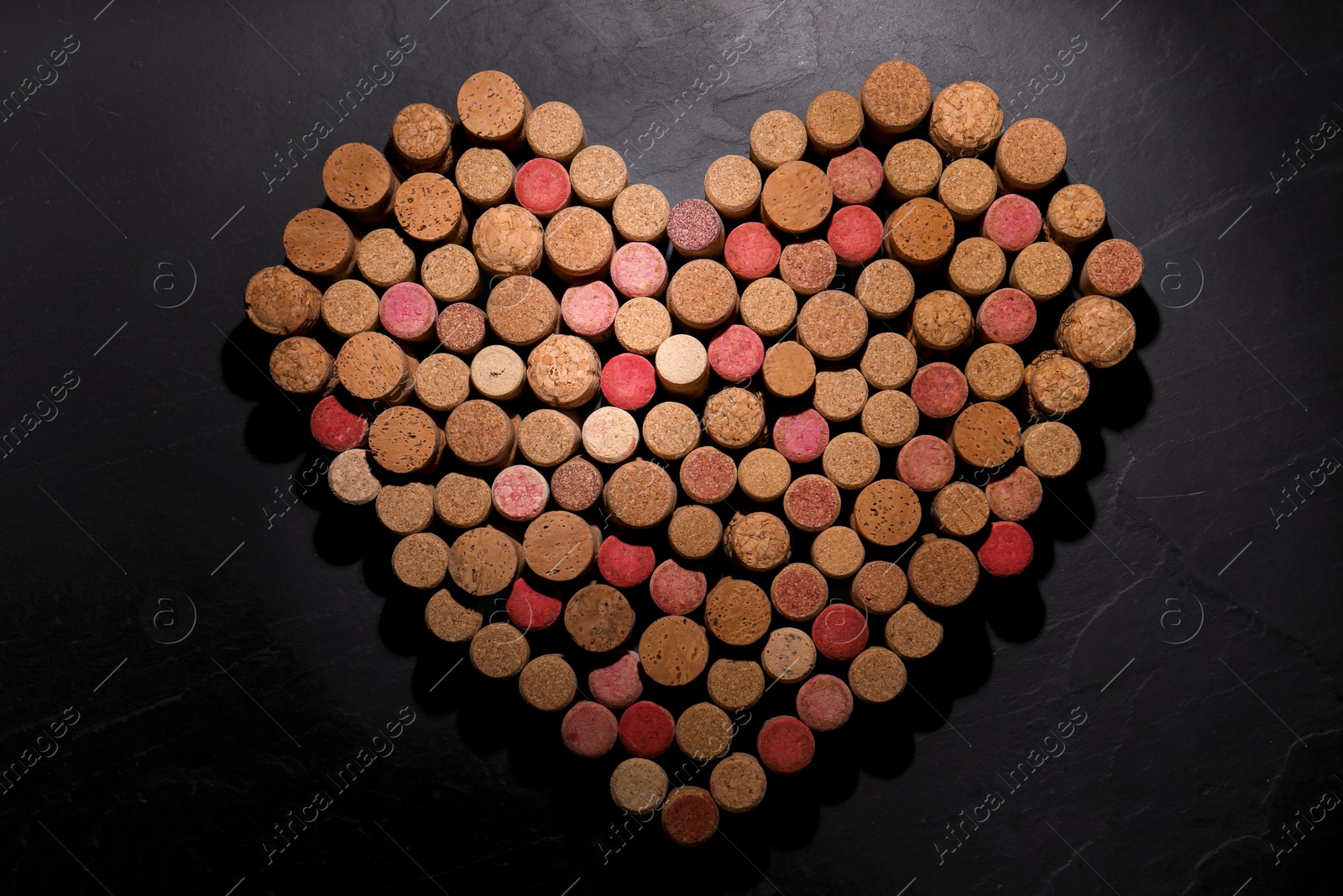 Photo of Heart made of wine bottle corks on black table, top view