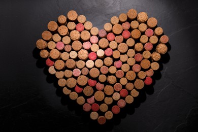 Photo of Heart made of wine bottle corks on black table, top view