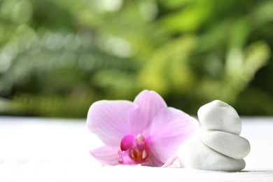Photo of Stack of white stones and beautiful flower on sand against blurred green background. Zen, meditation, harmony