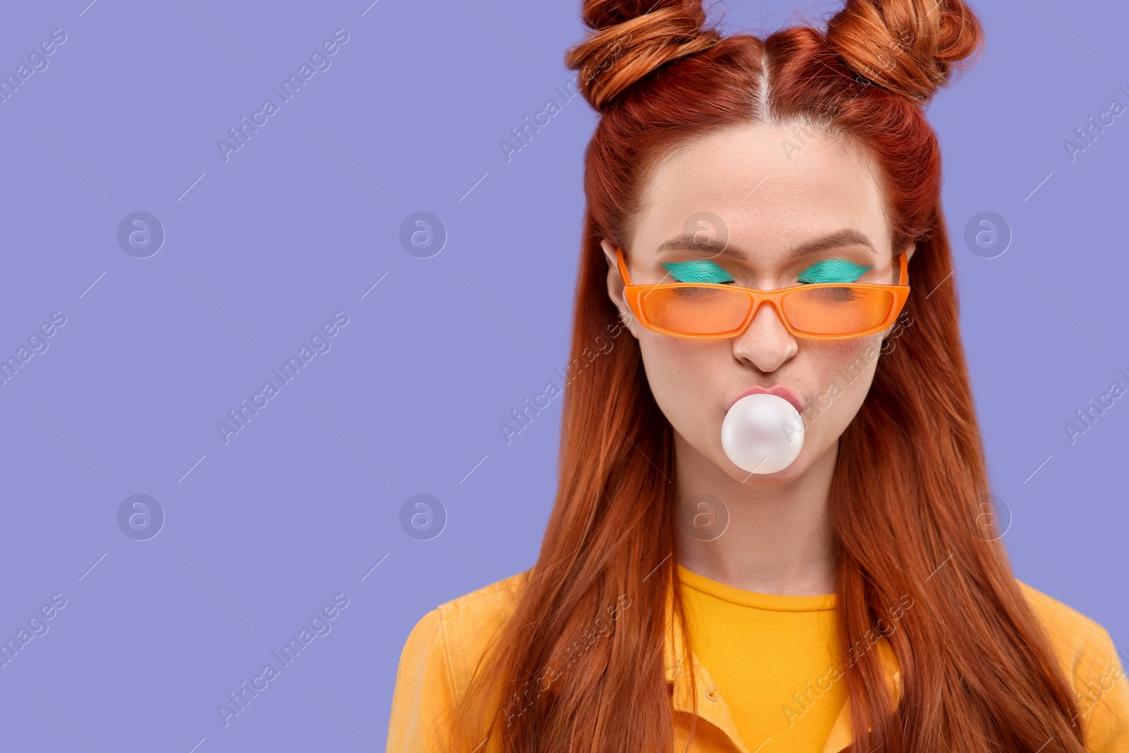 Photo of Beautiful woman with bright makeup and closed eyes blowing bubble gum on violet background. Space for text