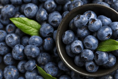 Photo of Tasty fresh blueberries with green leaves and bowl, top view