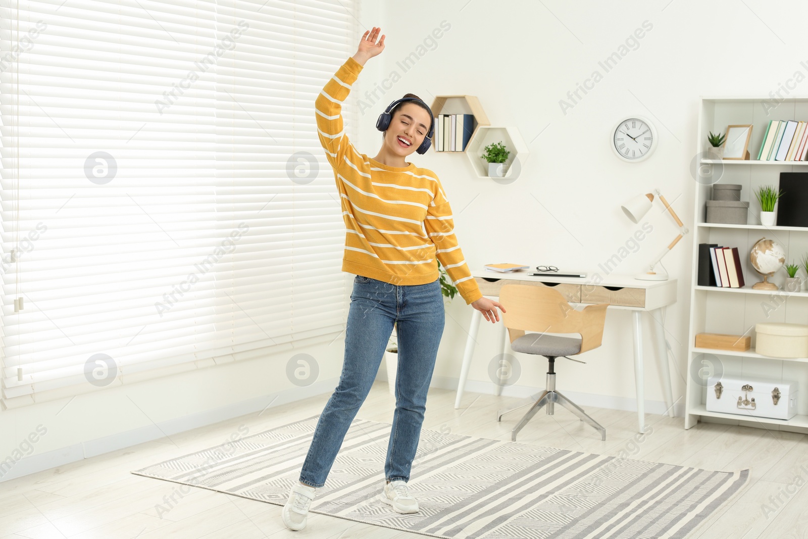 Photo of Happy woman in headphones listening music and dancing in cosy room