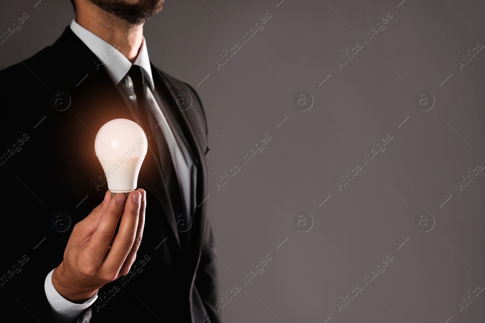 Photo of Businessman holding lamp bulb against gray background, closeup. Space for text