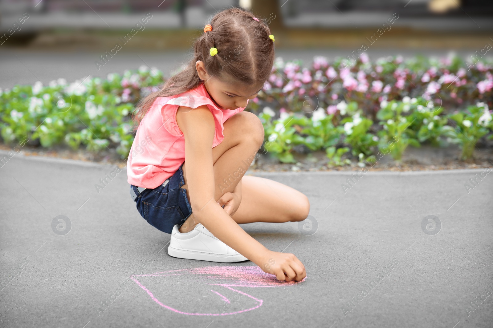 Photo of Little child drawing heart with chalk on asphalt