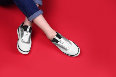 Woman in stylish shoes sitting on color background