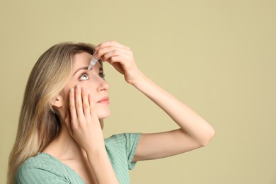 Photo of Young woman using eye drops on pale olive background