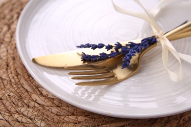 Photo of Cutlery, plate and preserved lavender flowers on wicker place mat, closeup