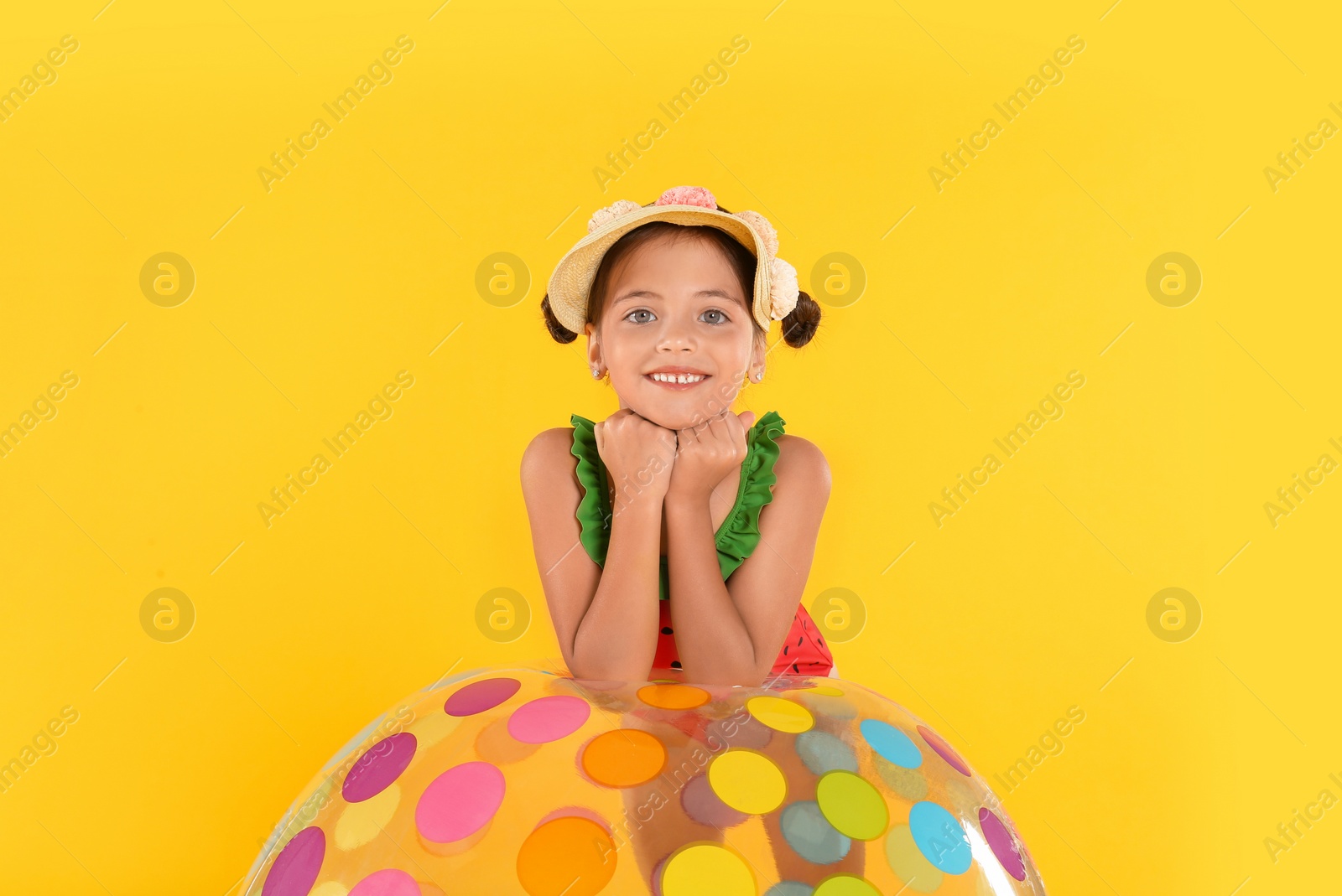 Photo of Cute little child in beachwear with bright inflatable ball on yellow background