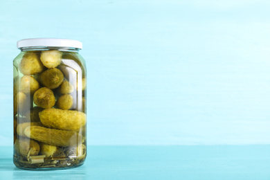 Photo of Glass jar of pickles on light blue wooden table. Space for text