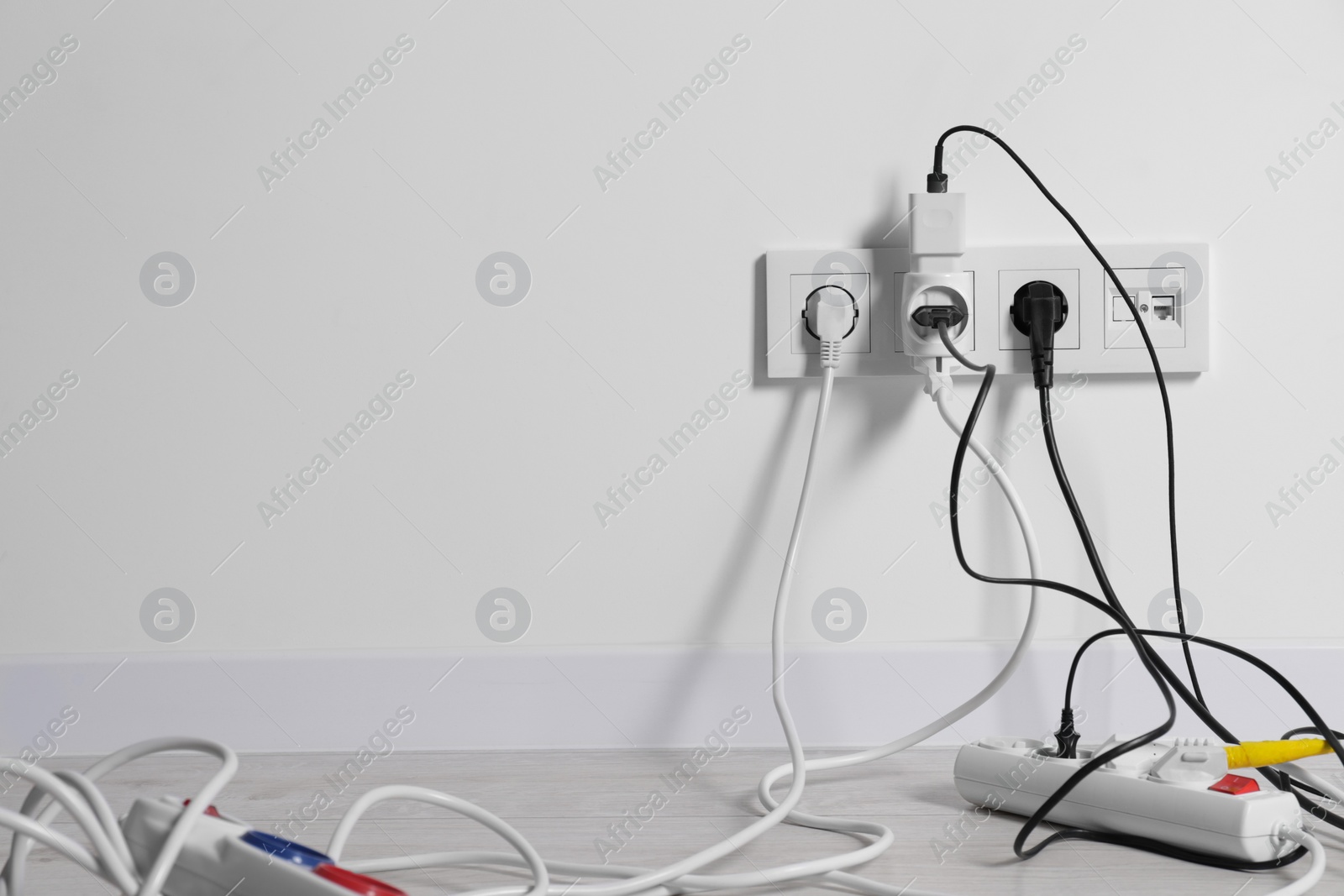 Photo of Different electrical plugs in sockets and power strip on floor indoors, space for text