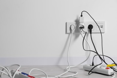 Photo of Different electrical plugs in sockets and power strip on floor indoors, space for text