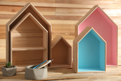 Painted house shaped shelves, brushes and plant on wooden table. Interior elements