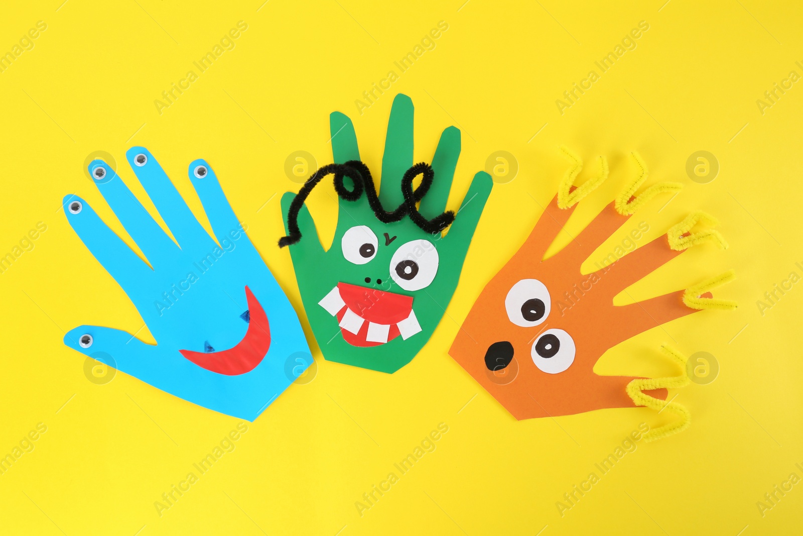 Photo of Funny hand shaped monsters on yellow background, flat lay. Halloween decoration