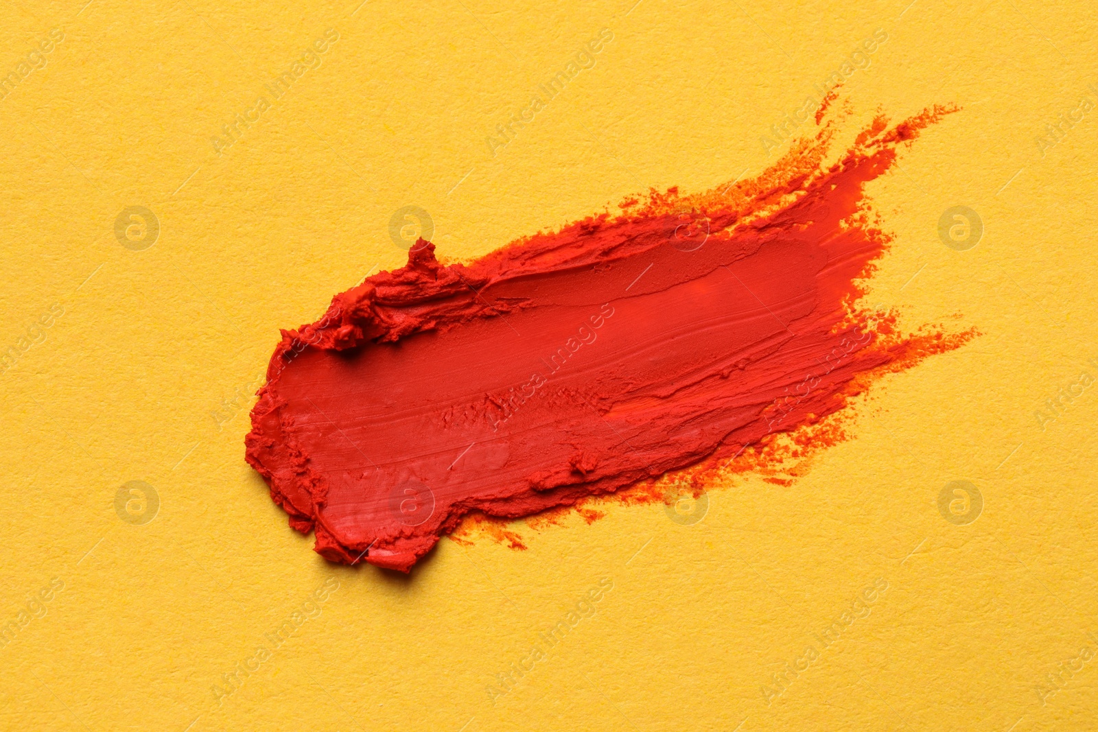 Photo of Smear of bright lipstick on yellow background, top view