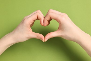 Photo of Woman showing heart gesture with hands on green background, closeup