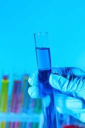 Photo of Scientist holding test tube with liquid on light blue background, closeup