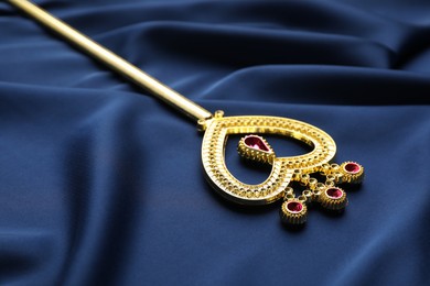 Photo of Beautiful golden magic wand on blue fabric, closeup