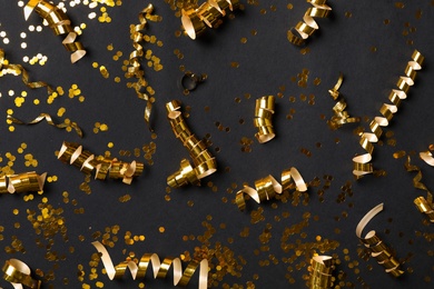 Shiny golden serpentine streamers and confetti on black background, flat lay