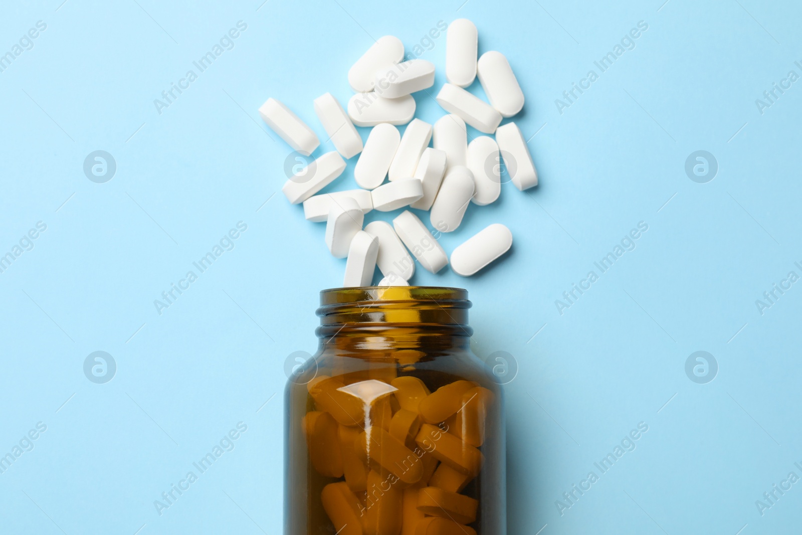 Photo of Vitamin pills and bottle on light blue background, top view