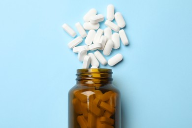 Photo of Vitamin pills and bottle on light blue background, top view