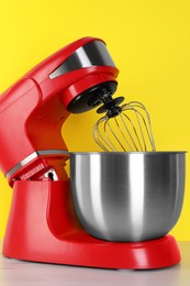 Photo of Modern red stand mixer on white wooden table against yellow background