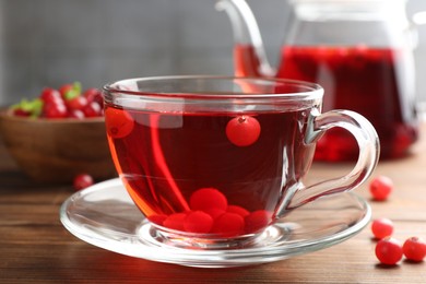 Photo of Tasty hot cranberry tea in glass cup and fresh berries on wooden table