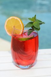 Glass of delicious cocktail on white wooden table near swimming pool, closeup. Refreshing drink