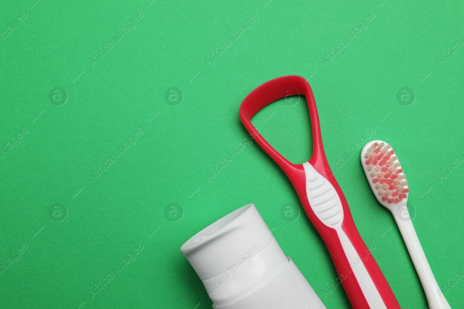 Photo of Red tongue cleaner, toothbrush and paste on green background, flat lay. Space for text