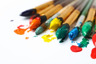 Photo of Brushes with colorful paints on white background, closeup