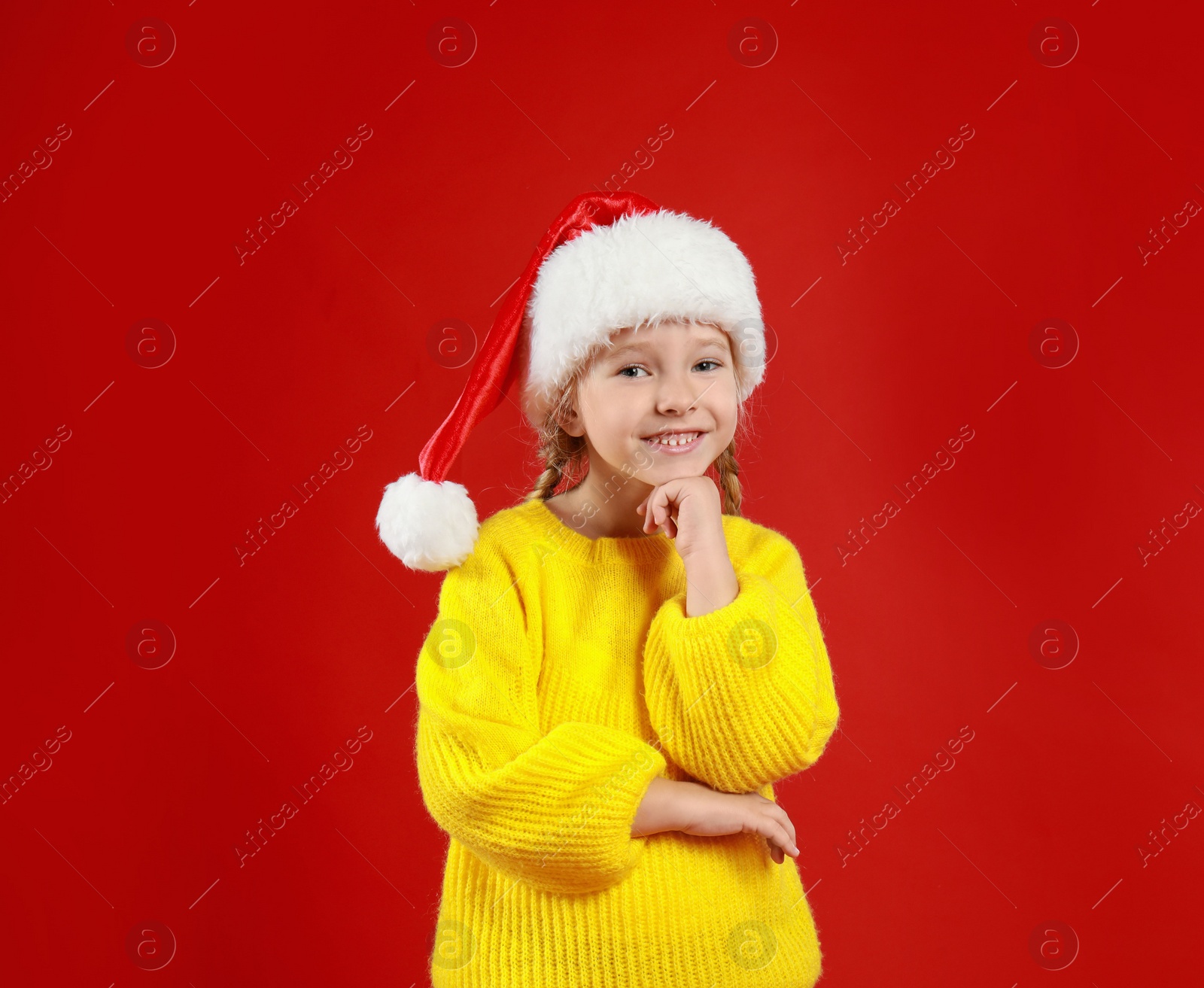 Photo of Cute little child wearing Santa hat on red background. Christmas holiday