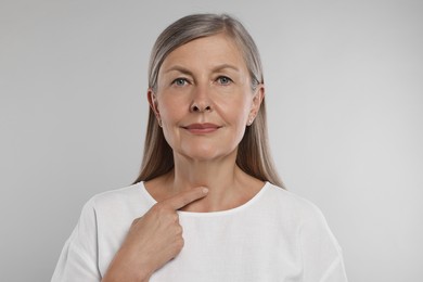 Photo of Endocrine system. Senior woman doing thyroid self examination on light grey background