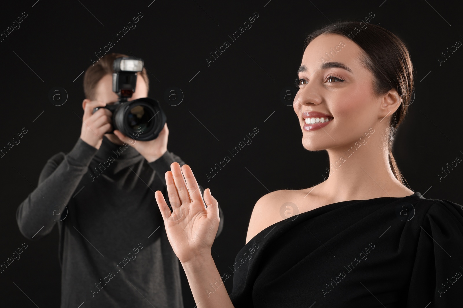 Photo of Photographer taking picture of beautiful woman on black background, selective focus
