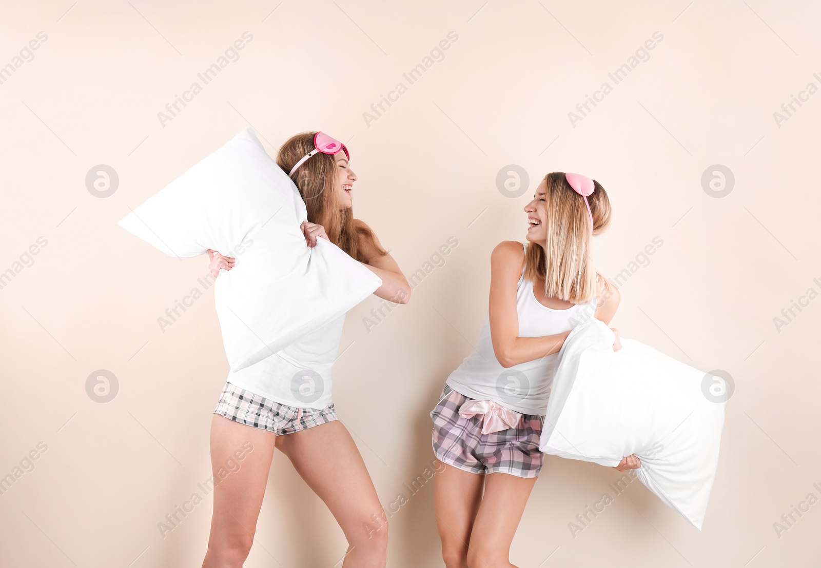 Photo of Two young women having pillow fight against color background