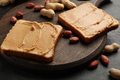 Photo of Tasty peanut butter sandwiches and peanuts on black table, closeup