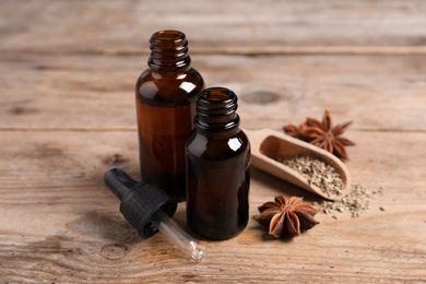 Photo of Bottles of essential oil, anise and seeds on wooden table