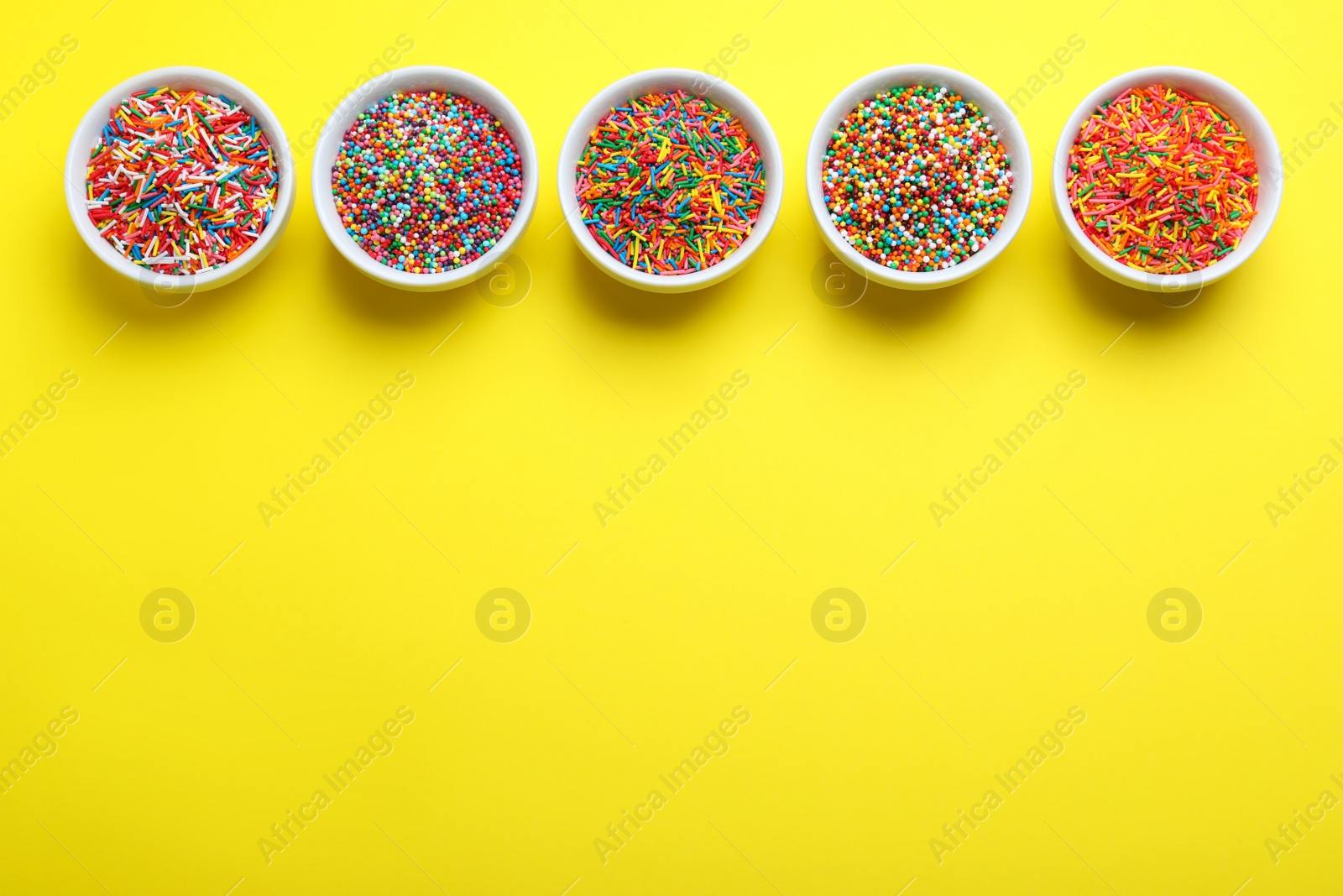 Photo of Colorful sprinkles in bowls on yellow background, flat lay with space for text. Confectionery decor