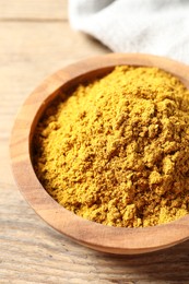 Photo of Dry curry powder in bowl on wooden table, closeup