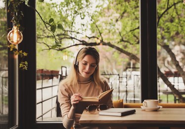 Photo of Woman listening to audiobook at table in cafe