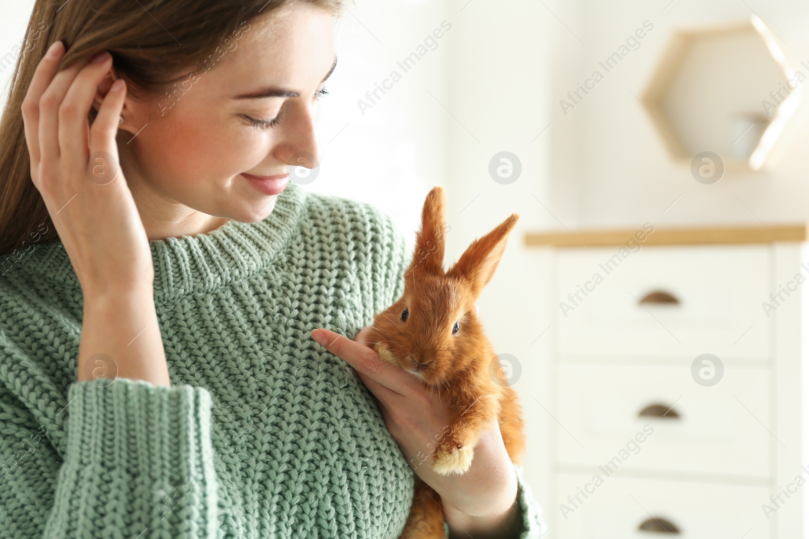 Photo of Young woman with adorable rabbit indoors. Lovely pet